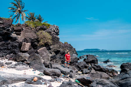 A young woman in a red swimsuit walks along the shore of the ocean on a sunny day.の写真素材