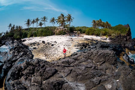 A woman in a red dress stands on the edge of a volcanic rock and looks at the seaの写真素材