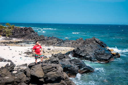 A woman in a colorful dress stands on a rock and looks at the sea
