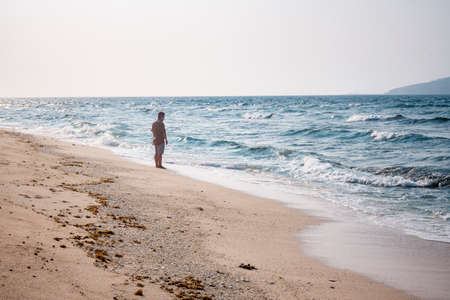 A woman walks along the seashore on a sunny day.の写真素材