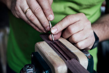Luthier's hands working and sanding a wood guitar piece. Shaping concept.