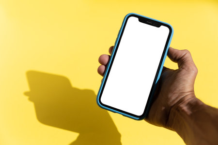 Black male hand holding a smart phone isolated blank screen yellow backgroundの写真素材