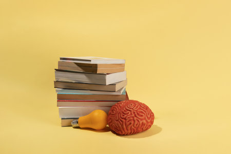 A brain, a bulb and books on yellow background, creative concept, ideas.