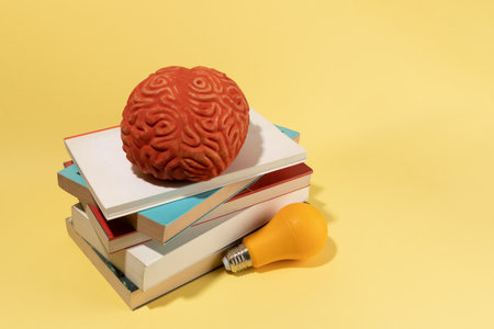 A brain, a bulb and books on yellow background, creative concept, ideas.