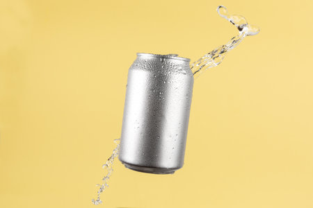 Aluminium beer or soda drinking can with water splash on light yellow background