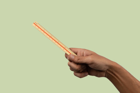 Male hand holding vintage ruler on light green background.の写真素材