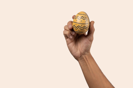 Male hand holding modern painted easter egg on beige background.の写真素材