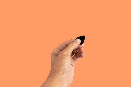 Black male hand holding a guitar pick isolated on orange backgroundの写真素材