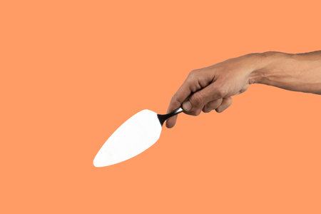 Black male hand holding a cake cutter knife isolated on orange backgroundの写真素材