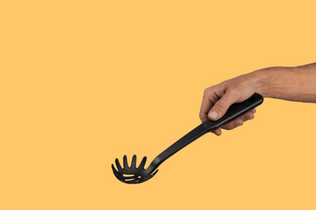 Black male hand holding plastic kitchen skimmer on yellow background.の写真素材