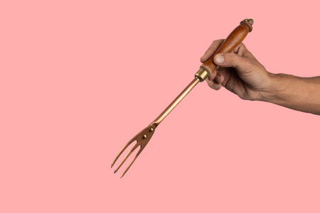 Black male hand holding a vintage brass meat fork on pink backgroundの写真素材