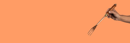 Black male hand holding a vintage brass meat fork on orange bannerの写真素材