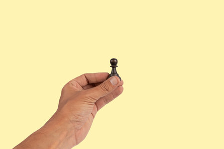 Isolated hand holding a chess figure on yellow background