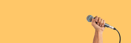 Black male hand holding a microphone isolated on yellow banner backgroundの写真素材