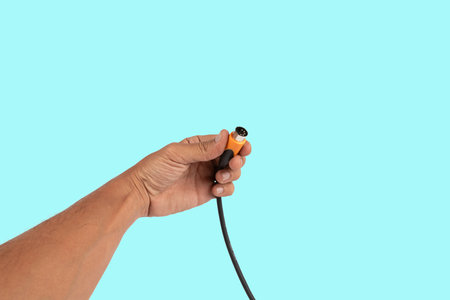Black male hand holding a MIDI audio cable isolated on cyan background