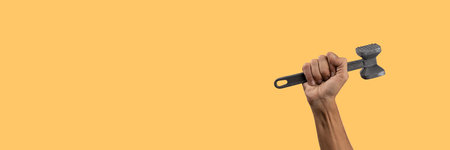 Black male hand holding a kitchen hammer isolated on yellow banner backgroundの写真素材