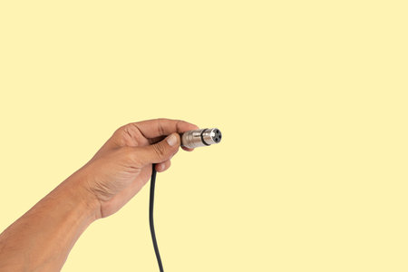 Male hand holding an XLR audio connector cable isolated on yellow backgroundの写真素材