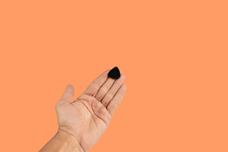 Black male hand holding a guitar pick isolated on orange backgroundの写真素材