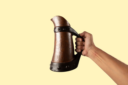 Male hand holding a medieval beer jar isolated on yellow backgroundの写真素材