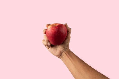 Male hand holding a red apple isolated on pink backgroundの写真素材