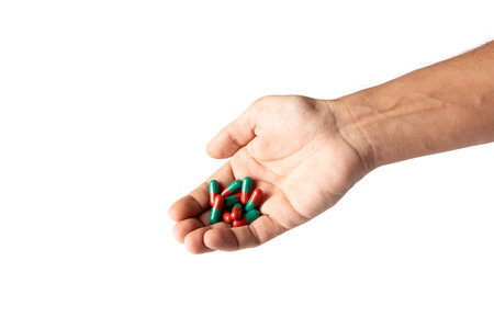 Male hand holding red medicine pill capsules isolated on white backgroundの写真素材