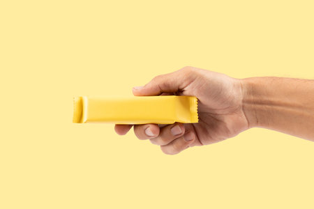 Male hand holding yellow snack bar mockup isolated on yellow background cutoutの写真素材