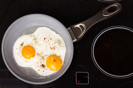 Frying pan with cooked two eggs and spicesの写真素材