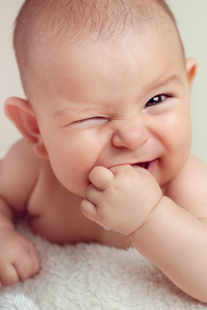 Small cute funny baby infant teething with face expression hands and fingers in mouth sore gums sootheの写真素材