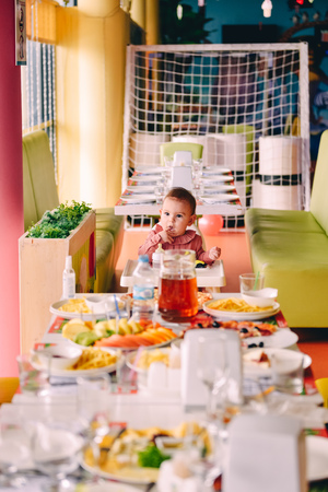Baby girl in pink in highchair in front of big fest table at birthday partyの写真素材