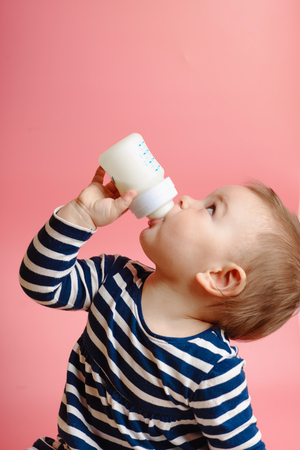 Portrait of a cute toddler drinking milk from the bottle, one year old food conceptの写真素材