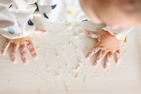 a little girl in a t-shirt and plate sitting in a childs chair eating with hands cereals with yogurt foodの写真素材
