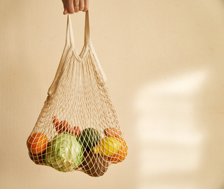 Woman hand holding a string shopping bag with vegetables, fruits in warm earthy tones, zero wasteの写真素材