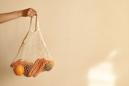 Woman hand holding a string shopping bag with vegetables, fruits in warm earthy tones, zero wasteの写真素材
