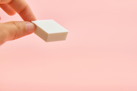 Rectangle cosmetic white sponge in hands on pink background, copy spaceの写真素材