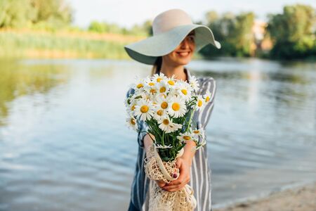 Chamomile bouquet in girls hands on river background. Happy florist concept. Calming teaの写真素材