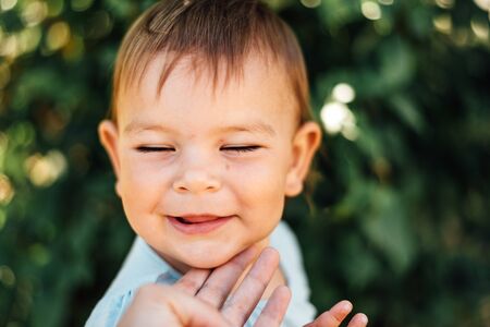 Happy baby with closed eyes and mothers hand touching chin. Lifestyleの写真素材