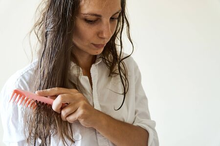 Beautiful woman brushing her wet messy hair after bath with comb. Thin hair porblemの写真素材