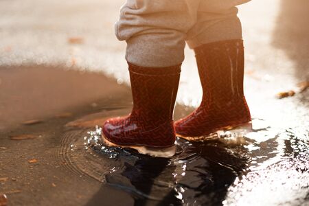 Little girl in red rainboots playing in puddle after rain. Happy fall childhood activity