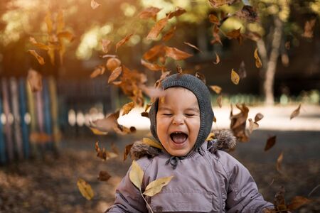 Little toddler boy in autumn park with leaves falling. Emotions of happiness and joy