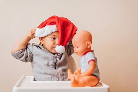 baby in Christmas bonnet dressing up the doll , on white background. copy spaceの写真素材