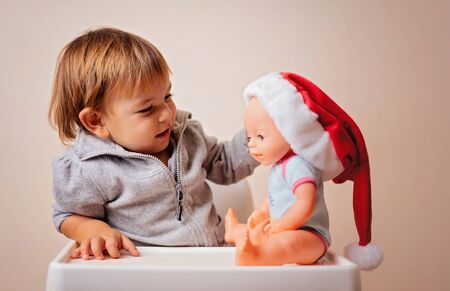 baby in Christmas bonnet dressing up the doll , on white background. copy space