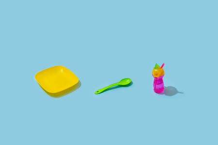 Isomentric minimal objects of baby food cutlery - plate, spoon, bottle. Blue background, harsh lightの写真素材