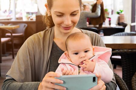 Mother and baby outddors in a restaurant watching carttons, making selfie
