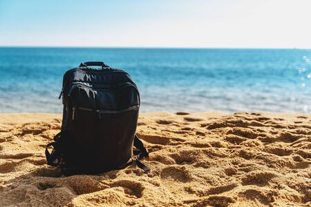 Black backpack on sand and sea. Hiking or tourism. Summer vacation