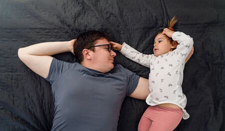 Father and his baby toddler girl laying on bed and hugging in the morning. Bonding time togetherの写真素材