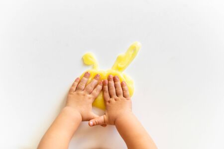 Top view of kids hand and yellow slime on white background. Toddler activity. Motor skills. Homemade clayの写真素材