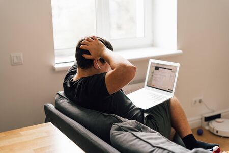 Young caucasian businessman working from home in living room on sofa. Reading bad news, get bank...
