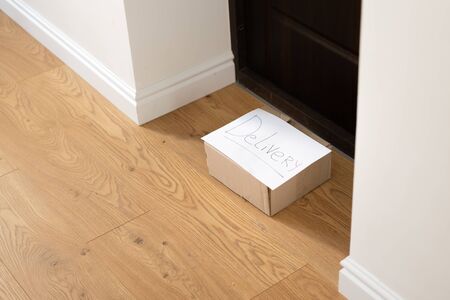 Young woman at home in gloves and mask taking delivery box from the floor. Contactless delivery...
