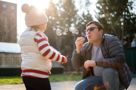 Caucasian man with his child blowing soap bubbles outside. Slow motion. Weekend activity with toddler, backyardの写真素材