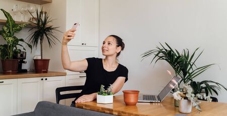YOung millennial woman working from home. Room with plants. Freelancer florist